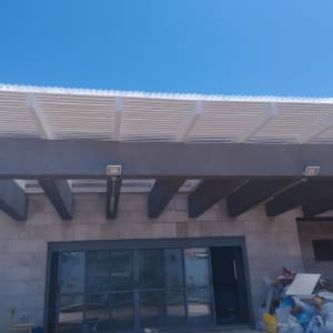 פרגולה מעץ לבן מעל מבנה עם קורות אפורות