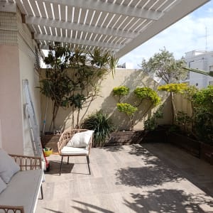 מרפסת עם צמחים ועציצים תחת פרגולה לבנה