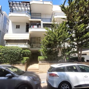 בניין מגורים עם עצים ומכוניות בחזית