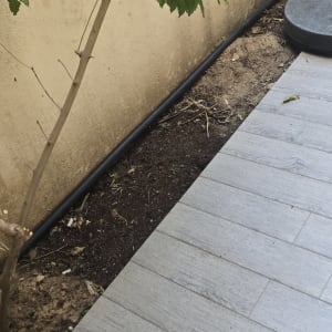 צינור צנרת שחור המותקן באדמת הגינה לצד שביל מרוצף
