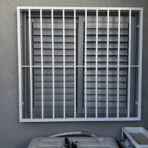 סורג מתכת על חלון עם תריסים אפורים