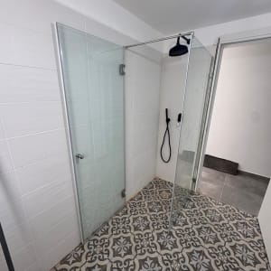 מקלחון זכוכית עם ראש מקלחת שחור ורצפת אריחים מעוצבת