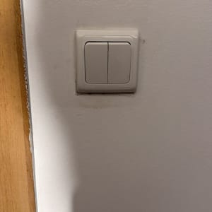 מתג חשמלי על קיר לבן ליד דלת עץ