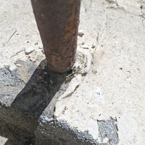 תקריב של צינור חלוד החודר למשטח בטון עם פגיעה באיטום