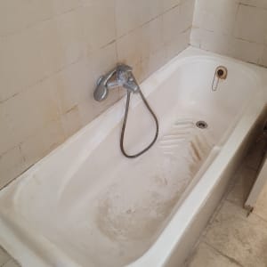 אמבטיה מלוכלכת עם כתמים, ברז ומקלחת יד