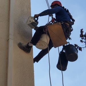 אדם עם קסדה צובע קיר חיצוני בעזרת מברשת