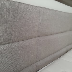 ראש מיטה מרופד בבד אפור ליד מזרן לבן