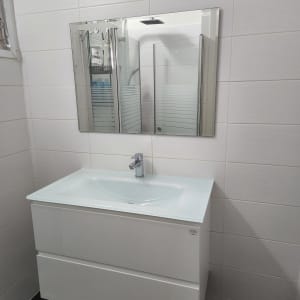 כיור לבן עם ברז מתכת ומראה על הקיר