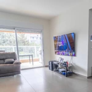 סלון עם טלוויזיה על קיר גבס ומדף עם מכשירים אלקטרוניים