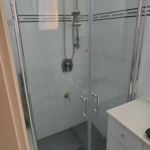 מקלחון זכוכית עם ראש מקלחת מתכתי וקירות אריחים לבנים