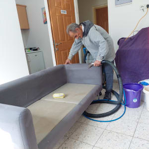 אדם מנקה ספה עם שואב אבק, דלי וסבון