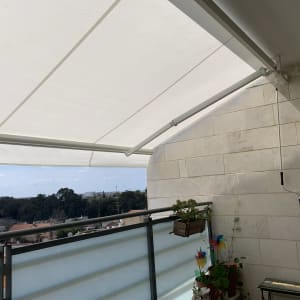 סוכך לבן מותקן על קיר מרפסת עם זרועות מתכת