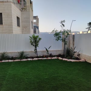 גינה עם דשא, עצים ופרחים ליד גדר לבנה