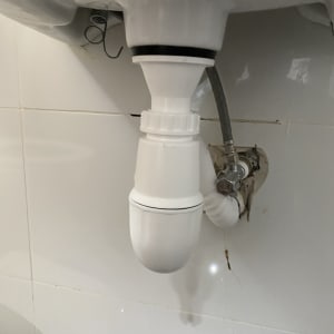 צינור ניקוז לבן מתחת לכיור עם נזילה קלה