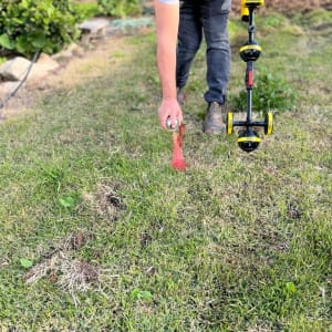 אדם מסמן דשא עם ספריי אדום ומכשיר איתור צינורות