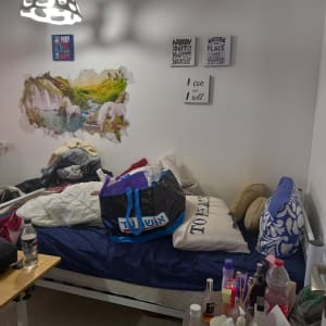 חדר מבולגן עם מיטה, שקיות ומוצרי טיפוח על שולחן