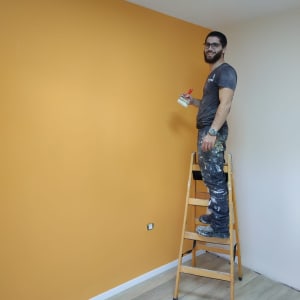 אדם צובע קיר בצבע כתום בעזרת מברשת.