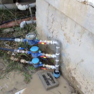 צנרת מים עם מדי מים וברזים ליד קיר בטון