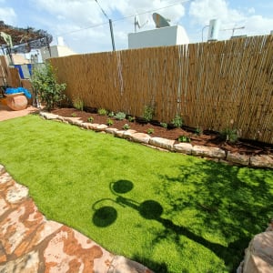 גינה עם דשא ירוק, ערוגת פרחים וגדר במבוק