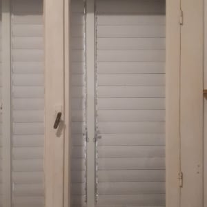 חלון זכוכית עם תריסים סגורים במסגרת עץ לבנה