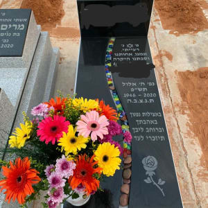 מצבה שחורה עם כיתוב בעברית ופרחים צבעוניים