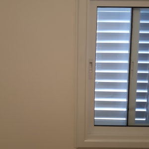 חלון אלומיניום עם תריסים סגורים על קיר לבן