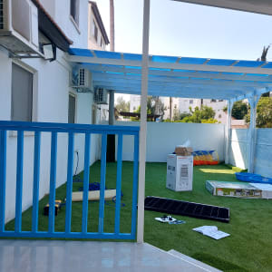 חצר עם דשא סינתטי, פרגולה כחולה וקרטונים על הרצפה