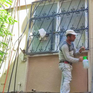 אדם עם מיכל ריסוס ליד חלון עם סורגים