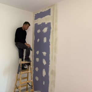 אדם עומד על סולם ליד קיר גבס בתהליך תיקון