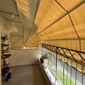 מרפסת עם סוכך צהוב מעל מעקה ברזל ירוק.