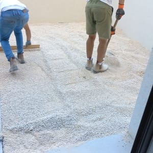 שני אנשים מפזרים חצץ בגינה עם כלים