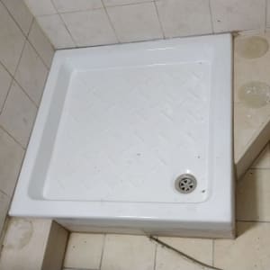 אגנית מקלחון לבנה מותקנת בפינת חדר רחצה מרוצף ומחופה אריחים