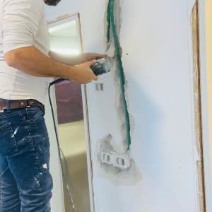 אדם קודח בקיר עם כלי עבודה חשמלי