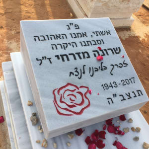 מצבה עם כיתוב בעברית ופרחים אדומים