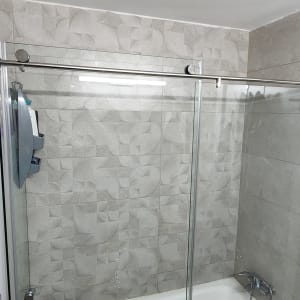 מקלחון זכוכית עם ברז מתכת וקיר אריחים אפור