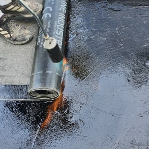 אדם משתמש במבער להדבקת יריעת איטום על גג