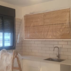 מטבח בשיפוץ עם ארונות מכוסים בניילון וסולם