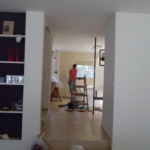 אדם צובע קיר עם רולר, סולם וחומרי בנייה