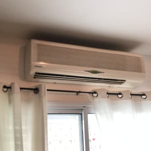 מזגן מותקן על קיר מעל חלון עם וילונות