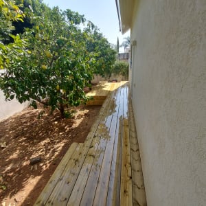 דק עץ ליד קיר בית עם עצי פרי