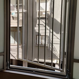 חלון פתוח עם סורגי מתכת מול בניין סמוך