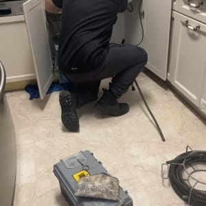 אינסטלטור עובד מתחת לכיור עם כלי עבודה וצינור