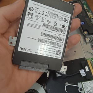 כונן קשיח Sandisk מוחזק ביד ליד מחשב פתוח