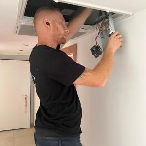 אדם מתקין מזגן בתקרה עם כלי עבודה