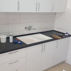 מטבח עם כיור כפול, כלים וחומרי ניקוי על השיש