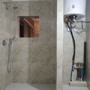 חדר רחצה עם אריחים חדשים, דוד שמש וצנרת חשופה.