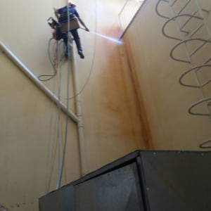 אדם תלוי על חבלים מנקה קיר עם צינור מים