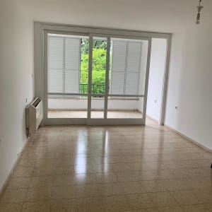 חדר ריק עם רצפת אריחים, חלון גדול ותריסים