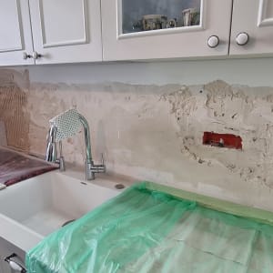 אדם מתקין אריחים על קיר מטבח במהלך שיפוץ