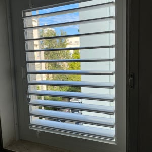 תריסים לבנים פתוחים בחלון עם נוף חיצוני